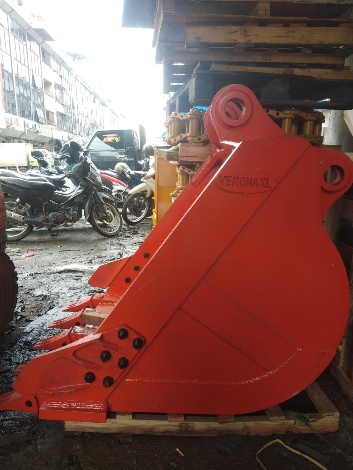 Finished red excavator bucket with bolt-on cutting edge, on a pallet