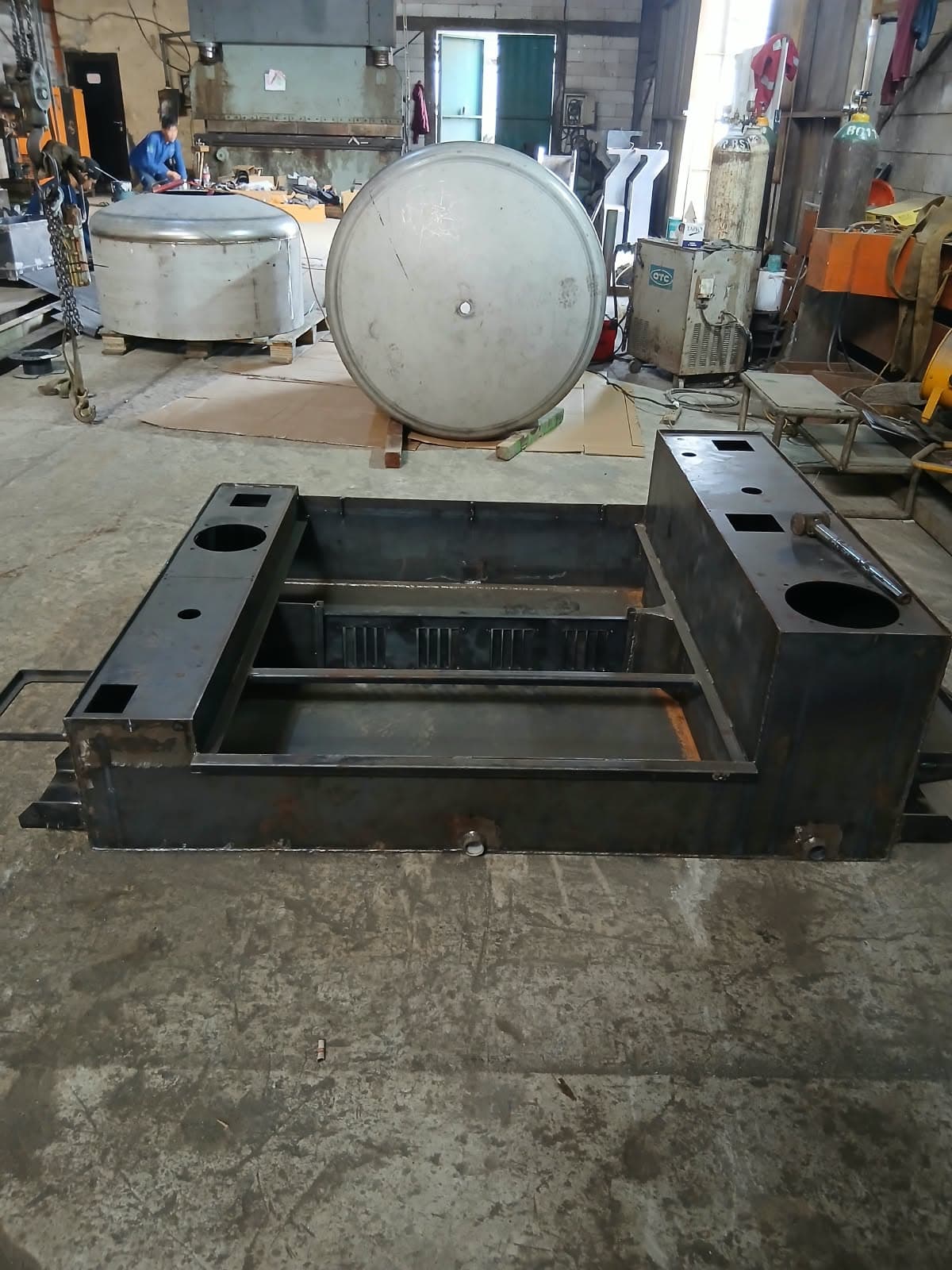 Machined steel base frame on the shop floor, stainless tank heads behind it